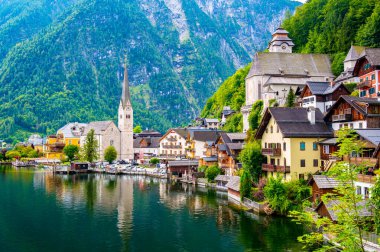 Hallstatt şehrinin ünlü manzarası ve göl kenarındaki kilise. Arka planda dağlar. Yaz yağmurlu günü, yumuşak renkler, bulutlu hava.