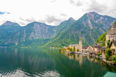 Hallstatt şehrinin ünlü manzarası ve göl kenarındaki kilise. Arka planda dağlar. Yaz yağmurlu günü, yumuşak renkler, bulutlu hava.
