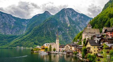 Hallstatt şehrinin ünlü manzarası ve göl kenarındaki kilise. Arka planda dağlar. Yaz yağmurlu günü, yumuşak renkler, bulutlu hava.