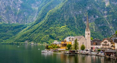 Hallstatt şehrinin ünlü manzarası ve göl kenarındaki kilise. Arka planda dağlar. Yaz yağmurlu günü, yumuşak renkler, bulutlu hava.