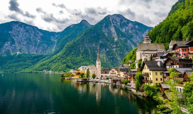 Hallstatt şehrinin ünlü manzarası ve göl kenarındaki kilise. Arka planda dağlar. Yaz yağmurlu günü, yumuşak renkler, bulutlu hava.