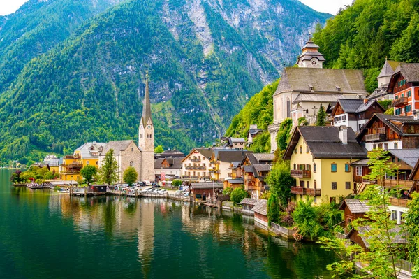 Hallstatt şehrinin ünlü manzarası ve göl kenarındaki kilise. Arka planda dağlar. Yaz yağmurlu günü, yumuşak renkler, bulutlu hava.