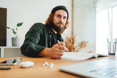 Genç hippi öğrenci uzaktan derste internetten ders çalışıyor. Sakallı adam üniversitede okurken ev ödevi yapıyor.