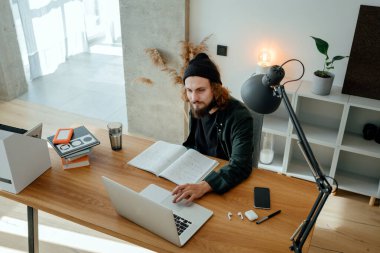 Uzaktan derslere girerken genç öğrencilerin online çalışmalarının en üst görüntüsü. Sakallı hippi üniversitede okurken ev işi yapıyor.