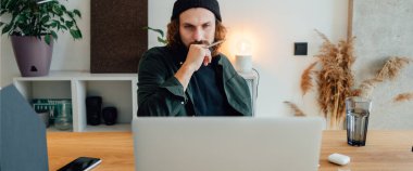 Genç hippi öğrenci uzaktan derste internetten ders çalışıyor. Sakallı adam üniversitede okurken ev ödevi yapıyor.