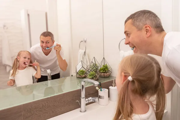 Papa leert dochter tanden poetsen met tandenborstel en tandpasta in de badkamer — Stockfoto