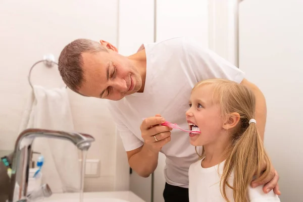 Papa reinigt dochters tanden met een tandenborstel in de badkamer, meisje glimlachen — Stockfoto