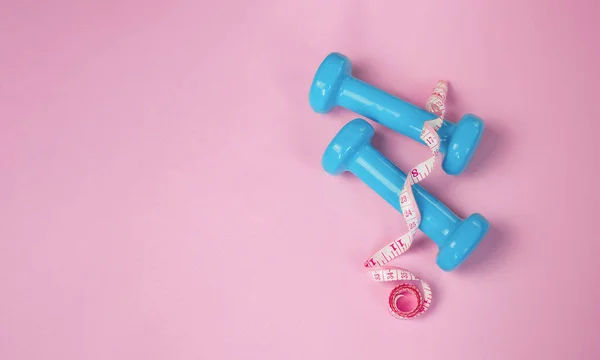 Top view: blue female dumbbells and measuring tape on a light blue background — 图库照片