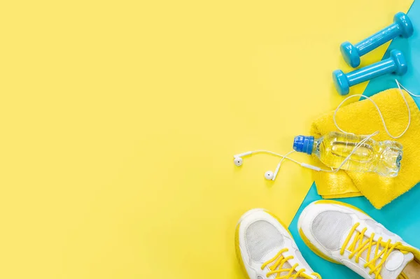 Yellow background on a sports theme, blue dumbbells, sneakers, headphones, water — 图库照片