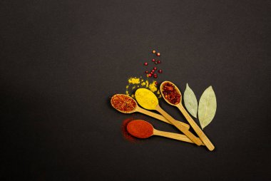 On a black background, on the right, there are four wooden spoons with spices.