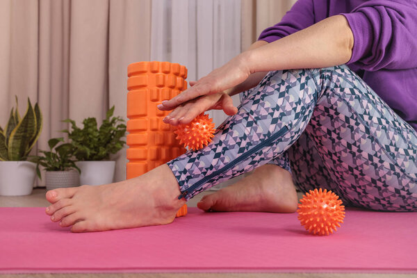 girl sits on floor and massages herself with prickly ball to relax and circulate