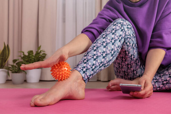 girl sits on floor and massages herself with prickly ball to relax and circulate