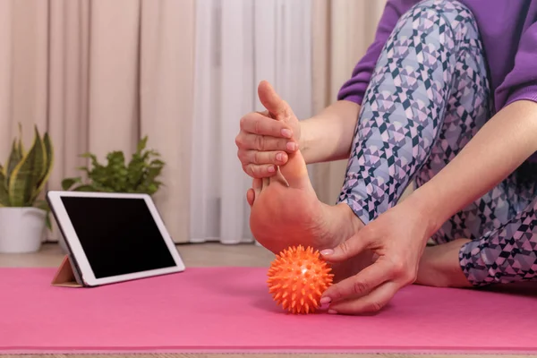 girl sits and massages her foot with a prickly ball to relax, looks at the ipad
