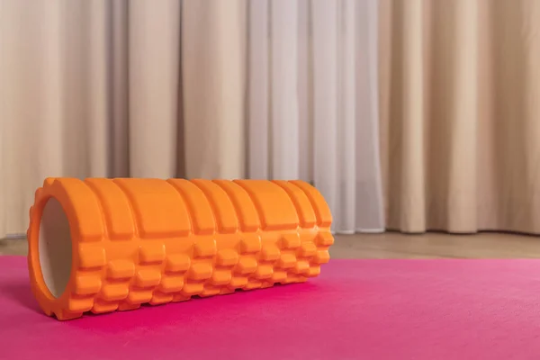 Pembe arka planda, evde miyofasyal masaj için büyük turuncu rulo yakın plan.