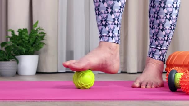 Close-up dos pés de uma menina dando-se uma massagem nos pés com uma bola verde — Vídeo de Stock