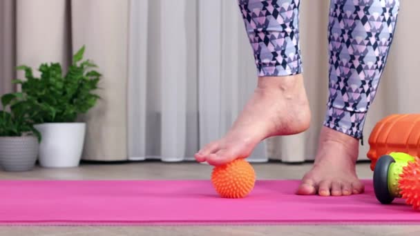 The girl stands on the floor and massages herself with a prickly ball to circulate blood — Stock Video