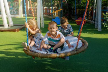 Güneşli bir yaz gününde çocuklar parkta salıncakta sallanır.