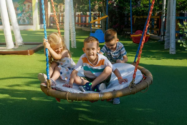 Op zonnige zomerdag schommelen kinderen op een schommel in een speeltuin in een openbaar park — Stockfoto