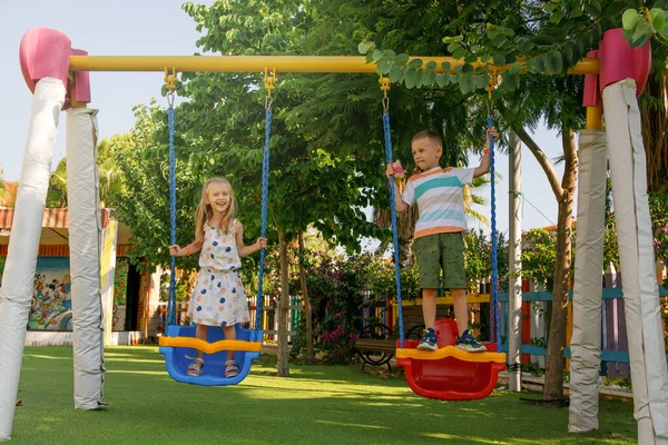 Op zonnige zomerdag, jongen en meisje schommelen op schommel in de speeltuin in het park — Stockfoto