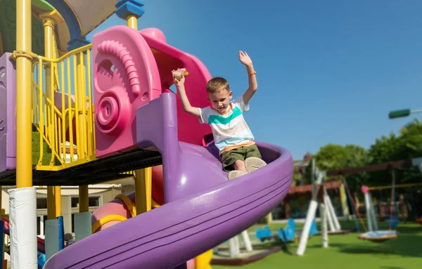 Op zonnige zomerdag glijdt een jongen van een glijbaan in een speeltuin in een openbaar park — Stockfoto