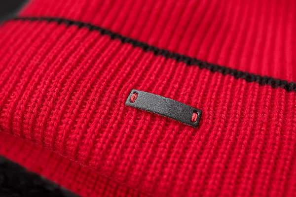 Detalle de un sombrero rojo brillante de punto con una etiqueta de cuero en blanco, maqueta, primer plano. — Foto de Stock