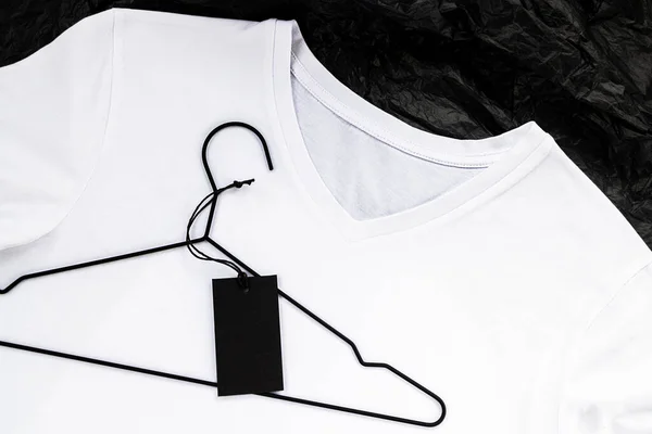 Weiße T-Shirt-Attrappe aus Baumwolle. Platz für ein Logo oder Etikett, Nahaufnahme. Schwarzes Etikett auf einem Kleiderbügel. — Stockfoto