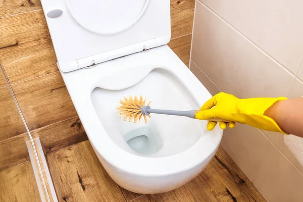 Close-up, tangan perempuan dalam sarung tangan kuning memegang pembersih toilet dalam botol biru — Stok Foto