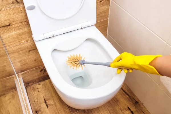 Close-up, a female hand in a yellow glove holds a toilet cleaner in a blue bottle Stock Image