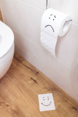 Duvarda üzgün yüzlü tuvalet kağıdı, yerde komik yüzlü kağıt.