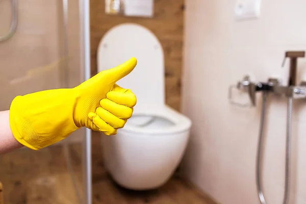 Primer plano de una mano en un guante amarillo en el fondo del baño — Foto de Stock