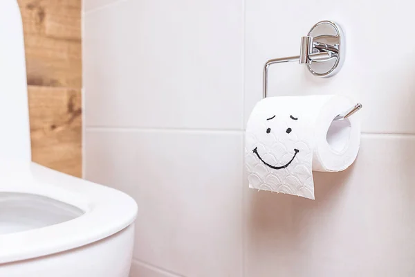 Um rolo de papel higiênico com um rosto feliz pendurado em uma parede branca no banheiro — Fotografia de Stock