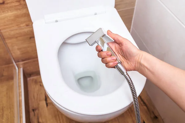 Primer plano, en una mano femenina una ducha higiénica, sobre el fondo de un inodoro moderno — Foto de Stock