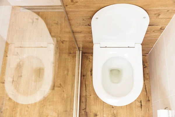 Pemandangan atas, mangkuk toilet putih bersih dengan penutup terbuka di kamar mandi modern, dinding putih dan lantai kayu — Stok Foto