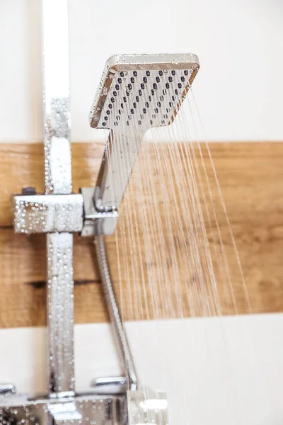 Primer plano de una ducha cromada, colgando de la pared, el agua que sale de ella — Foto de Stock
