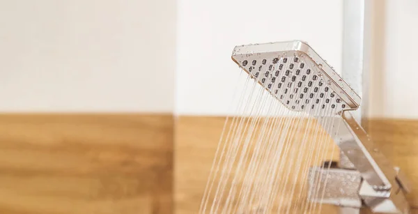 Primer plano, la ducha está colgando de una pared de cerámica, el agua está saliendo de ella — Foto de Stock
