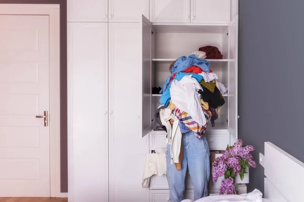 Elinde kocaman renkli buruşuk giysiler tutan genç bir kadının yakın çekimi. Arka plan odanın içi, büyük beyaz bir dolap. Kızın kafası görünmüyor, kopyala-yapıştır