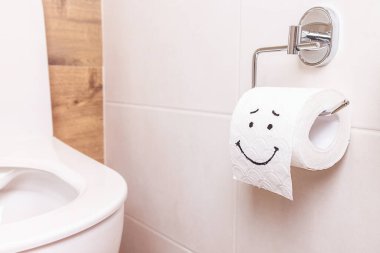 Tuvalet kağıdı rulosunun yakın çekimi. Banyoda duvarda komik bir gülen surat asılı. Sağlık konsepti, temiz banyo, mutlu hayat.