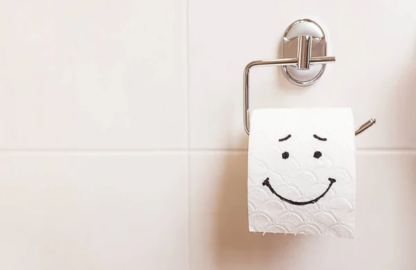 Tuvalet kağıdı rulosunun yakın çekimi ve banyo duvarında komik bir emoji asılı. Sağlık konsepti, temiz banyo, mutlu hayat. Dizaynınız ve metniniz için yapıştır