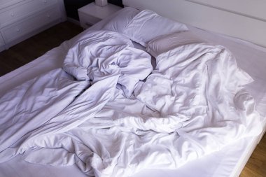 Sabahları kırışık, beyaz çarşaflı büyük çift kişilik yatak. Minimalist tarzda büyük, modern bir yatak odası. Konforlu ev konsepti, sabahın erken saatleri