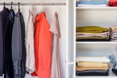 Yakından, bluzların, elbiselerin ve ceketlerin asılı olduğu beyaz bir dolap. Giysi seçimine ağır minimalist yaklaşım. Basit bir koleksiyon seçmek için bir stilistle çalışmak