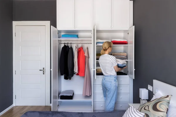 General layout of the room. girl neatly arranges clothes on the shelves in the closet. The concept of organizing space, order in the house, taking care of things, washing, ironing. Cleaning the house
