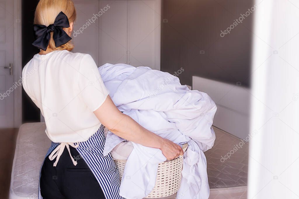 Close-up of a cleaning lady cleaning a hotel room and holding a basin of dirty linens to take to the laundry room and change for clean linens. The concept of cleaning, washing, ironing,