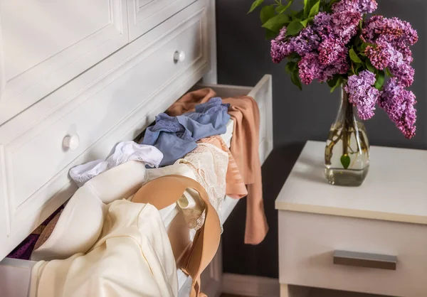 close-up drawers with clothes in a white closet in the apartment, put forward. Lingerie, lace panties, a bra and a tank top in a mess on a shelf. Sun rays in the morning, a bouquet of flowers nearby