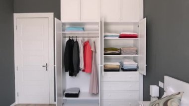 Yakından, bluzların, elbiselerin ve ceketlerin asılı olduğu beyaz bir dolap. Giysi seçimine ağır minimalist yaklaşım. Basit bir koleksiyon seçmek için bir stilistle çalışmak