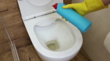 Yakın plan, kadın elleri tuvalet ve banyoyu dezenfekte etmek için sıvı deterjanla koruyucu sarı eldivenler giyiyor. Mavi bir temizlik şişesinin maketi. Hijyen, temizlik ya da umumi alan kavramı.