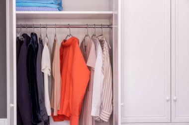 Yakından, bluzların, elbiselerin ve ceketlerin asılı olduğu beyaz bir dolap. Giysi seçimine ağır minimalist yaklaşım. Basit bir koleksiyon seçmek için bir stilistle çalışmak