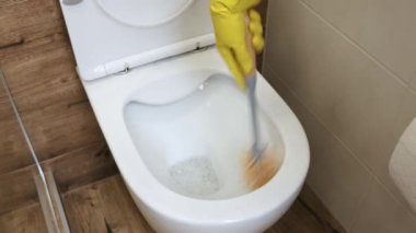 Yakın plan, kirli bir klozet, koruyucu sarı eldivenli bir el tuvalet fırçasıyla klozeti temizliyor. Odanın temizlenmesi ve dezenfekte edilmesi, sterilizasyon, hijyen...