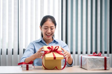 Mutlu kadın gülümsüyor ve hediye kutusuna bakarken kırmızı kurdeleyle hediye kutusunu açıyor. Çok heyecanlı ve mutlu bir şekilde Noel ve yeni yılı kutluyor.