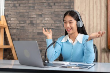 Kadın öğretmen kulaklık takıyor, dizüstü bilgisayar kullanıyor ve her ne kadar kamera ile webcam 'de video konferansında yeni dersler verirken matematik denklemlerini ve öğrencilere e-öğrenme kursunda fizik formülünü anlatıyor olsa da