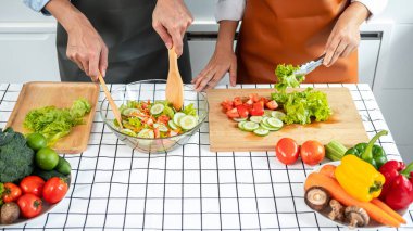 Asyalı romantik çift ahşap kesim tahtasına maşa ve domates koyarken genç adam kepçeyle evde sağlıklı yemek pişirmek için sebze salatası hazırlıyor.